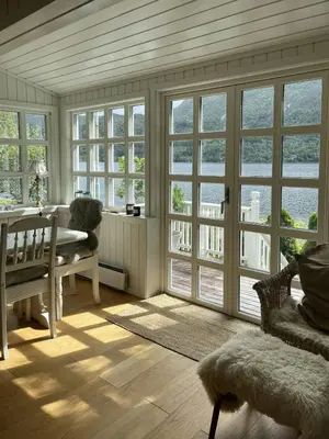 a living room with windows and a table and chairs at Cabin With Shoreline By Brusdalsvannet Lake in Ålesund
