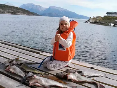 a little girl sitting on a dock with a bunch of fish at Charming sea house with sauna and private jetty in Ølve