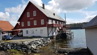 a large red and white building next to a body of water at Charming sea house with sauna and private jetty in Ølve