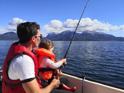 a man and a child in a boat holding a fishing pole at Charming sea house with sauna and private jetty in Ølve