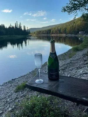 a bottle of wine and a glass sitting on a table next to a lake at Cabin With Great Fishing At Trysilfjellet in Jordet