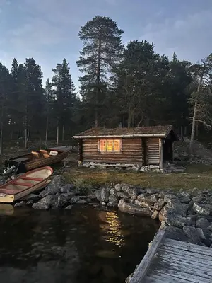 a cabin next to a body of water with a boat at Family cabin by the lake at Haugen, Femundsmarka in Elga