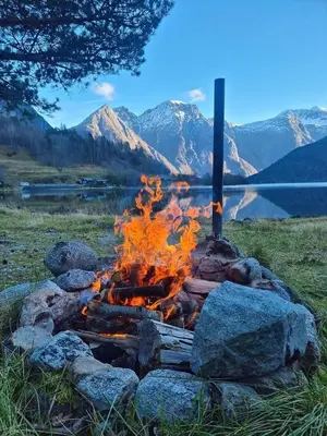 a fire pit with rocks and a lake and mountains at timber cabin Eresfjord med båt til leie in Øverås