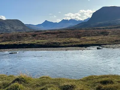a river in a field with mountains in the background at Koselig hytte med uthus på vakre Dovrefjell in Dovre