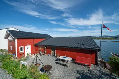 a red building with a picnic table and a flag at Eget hus i sjøkanten ved fjorden in Langevåg