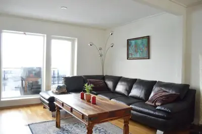 a living room with a black leather couch and a coffee table at Modern 3-story house by the sea & public transport in Trondheim