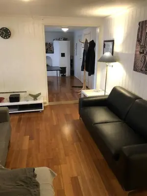 a living room with a black leather couch and a room with a kitchen at Trondhjemsvegen in Gjøvik