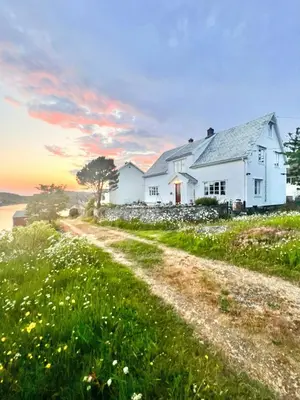 a white house on a hill with a dirt road at Historic Villa By The Sea In Solund in Hardbakke