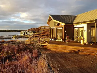 a house with a wooden deck next to a body of water at Seaside Dream Cabin With Jacuzzi in Steinsland