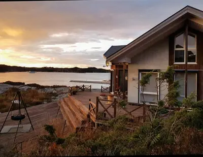 a house with a deck with a view of the water at Seaside Dream Cabin With Jacuzzi in Steinsland