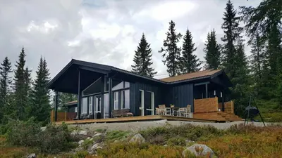 a black house with a large deck in the woods at Sunny Cabin With Panoramic Views At Sjusjøen in Sjusjøen