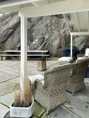 a patio with two wicker chairs and a stone wall at Charming Seaside Cabin With Views Over The Water