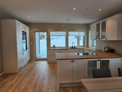 a large kitchen with white cabinets and wooden floors at Stor og ny leilighet med fjordutsikt in Sande