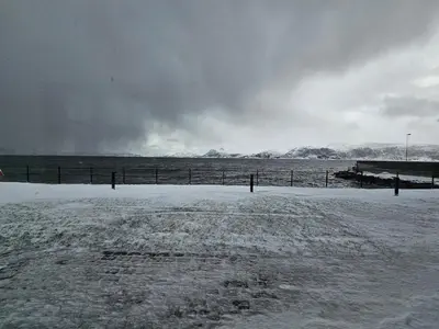 a field covered in snow with a fence and mountains at Stor og ny leilighet med fjordutsikt in Sande