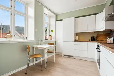 a kitchen with white cabinets and a table and chairs at Sjarmerende leilighet med utsikt, spa-bad og park in Bergen
