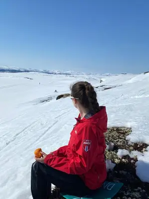 a woman sitting on the snow with a piece of food at Cozy cabin apartment, ski-in ski-out at Kvitfjell in Kvitfjell