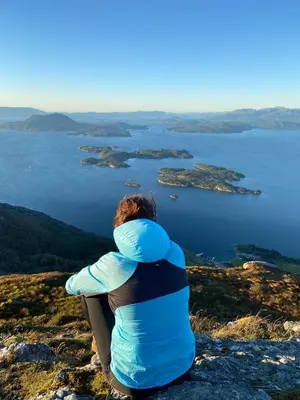 a woman sitting on top of a mountain overlooking a body of water at Holiday house Vindafjord Norway in Ølsvågen