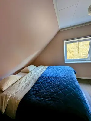 a bedroom with a blue comforter and a window at Fjord View Cabin Near Bergen & Nature in Grottveit