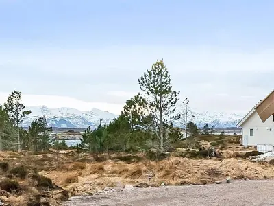 a white house in a field with mountains in the background at 6 person holiday home in Averøya in Karvåg