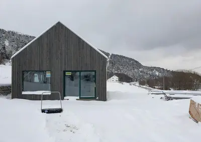 a building in the snow with a chair in front at Architect-Designed Cabin With Beach Nearby in Lensvik