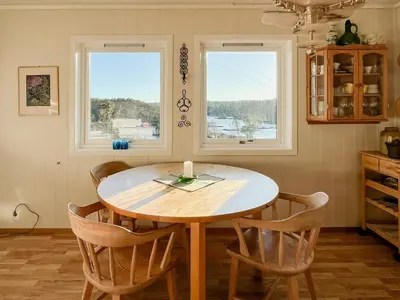 a dining room table with chairs and two windows at Seaside Cabin With Archipelago Views In Radøy in Bøvågen