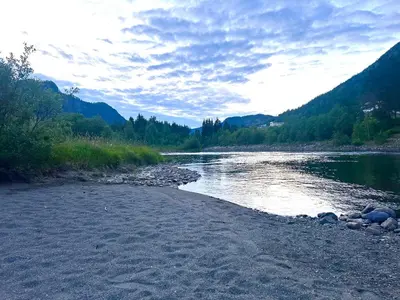 a river with a rocky shore with trees and mountains at Nord-Garthus gård leilighet 1 in Hølera