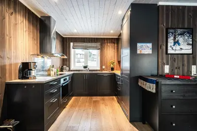 a kitchen with black cabinets and a wooden floor at Harmony in Geilo, modern and cozy cabin with jacuzzi in Geilo