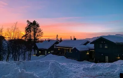 a house covered in snow with the sunset in the background at Family Cabin With Ski Inout In Rauland in Rauland