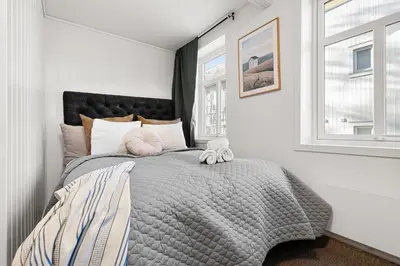 a bedroom with a bed with a gray comforter and windows at Nord Apartments in Trondheim