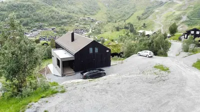 a black house with two cars parked next to a road at The Panoramic Chalet in Stranda
