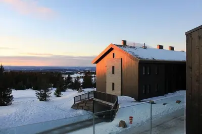 a building in the snow with the sun shining on it at Hafjelltoppen-New apartment with a beautiful view and high standard in Hafjell