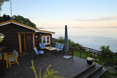a cabin with a deck with chairs and an umbrella at En perle i Trondheimsfjorden in Trondheim