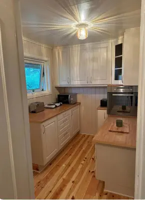 a kitchen with white cabinets and a wooden floor at Kjellerleilighet in Bjørge