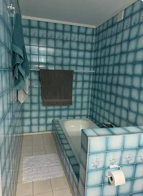 a blue tiled bathroom with a tub and a towel at Kjellerleilighet in Bjørge