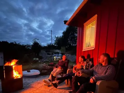 a group of people sitting around a fire in front of a red house at 6 person holiday home in KLOKKARVIK in Klokkarvik
