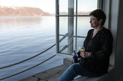 a woman sitting on a window sill with a glass of wine at Komfortable Ferieleiligheter med Sjøutsikt in Stadlandet