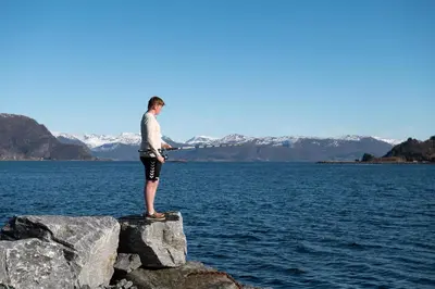 a man standing on a rock on a body of water at Komfortable Ferieleiligheter med Sjøutsikt in Stadlandet