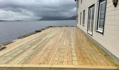 a wooden dock next to a building next to the water at Komfortable Ferieleiligheter med Sjøutsikt in Stadlandet