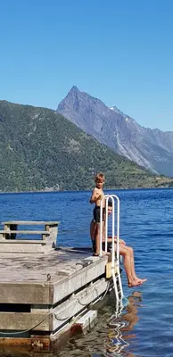 a man sitting on a dock in the water at Hytte Blåtind, Rekkedal Gjestegard - Sæbø in Sæbø