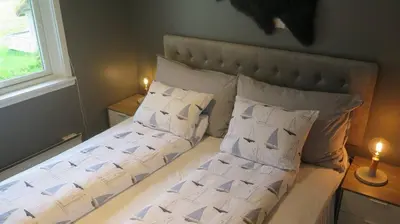 a bed with white sheets and pillows next to a window at Sara's Fjord View House in Stadlandet