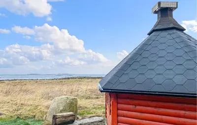 a red building with a black roof next to the ocean at Pet Friendly Apartment In Harøy in Steinshamn