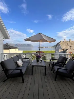 a deck with two couches and a table with an umbrella at Cozy house with sea view close to Ålesund in Havsteinen