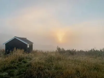 a foggy field with a smallshed on a hill with the sun poking out at Traditional Mountain Cabin Near Hallingskarvet in Torpo