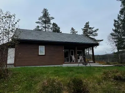 a small log cabin with a porch in a field at Flott familiehytte på Haukås i Strandebarm in Kvam