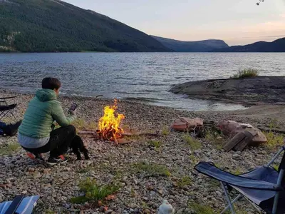 a person sitting next to a fire on a beach at Perla i Nordfjord in Emhjella