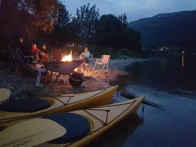 a group of people sitting around a campfire next to a river at Perla i Nordfjord in Emhjella