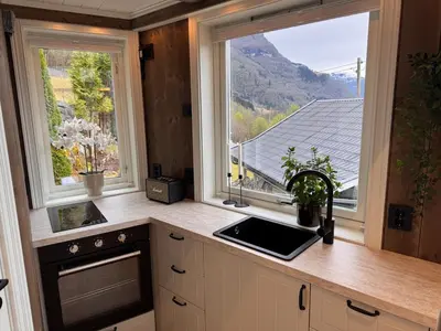a kitchen with a sink and two large windows at Fjord Cabin with Panoramic View & Private Balcony in Luster