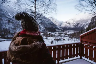 a person sitting on a fence looking at a snow covered mountain at Vinje Camping in Geiranger
