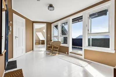 a living room with windows and a table and chairs at Rom i loftsleilighet med utsikt in Bergen
