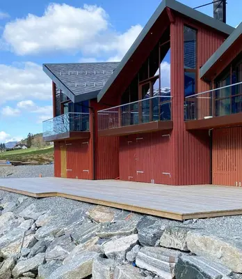 a red house with a wooden deck and a building at Near-Sea Boat House With Panoramic Views in Sykkylven
